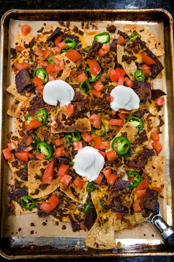 Ultimate Beef Nachos are oven crispy tortilla chips drenched in melted cheese, spicy meat and peppers. Perfect for game day, parties and a sheet pan dinner. #mustlovehomecooking