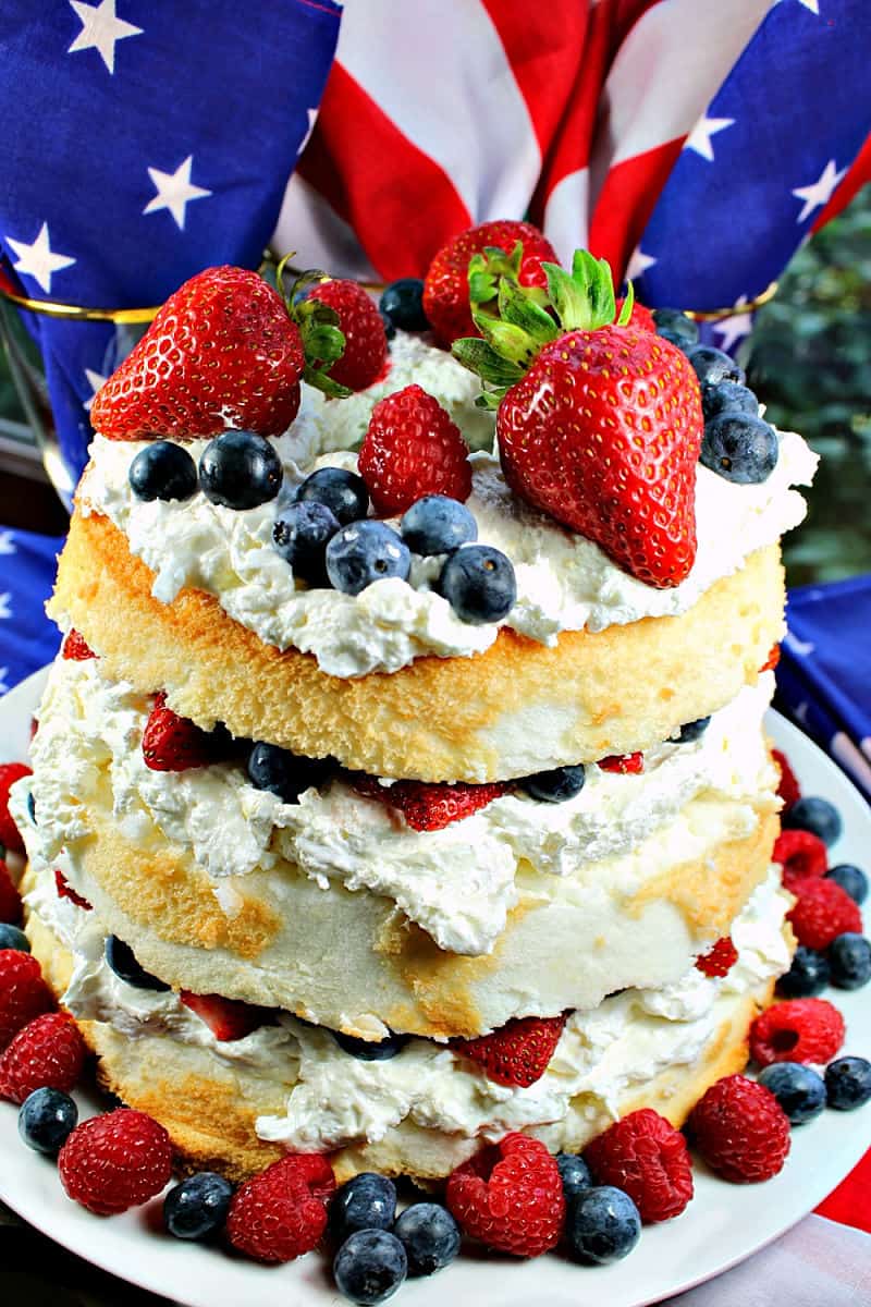 Patriotic Angel Food Cake is layers of fluffy angel food cake, stuffed with a cream cheese filling and then fruit mounded in the layers and on top. A perfect summer dessert! #mustlovehomecooking