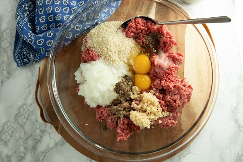 Ingredients for meatballs in glass mixing bowl