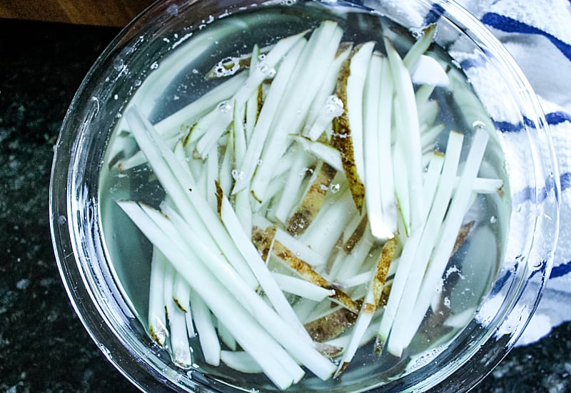 cut potatoes soaking in glass mixing bowl of water