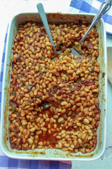 From Scratch Cola Baked beans in white baking dish with spoon