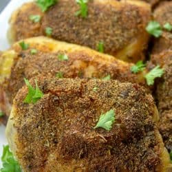 crispy oven baked chicken thigh on white platter with parsley