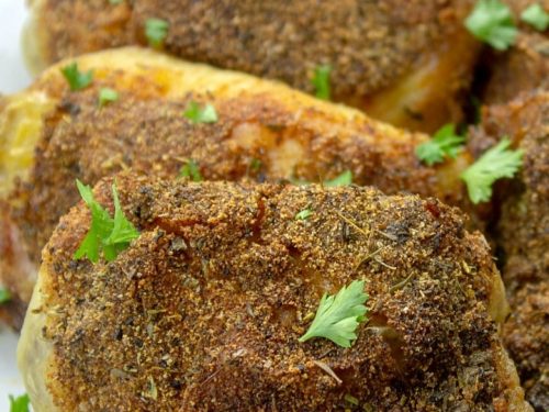crispy oven baked chicken thigh on white platter with parsley