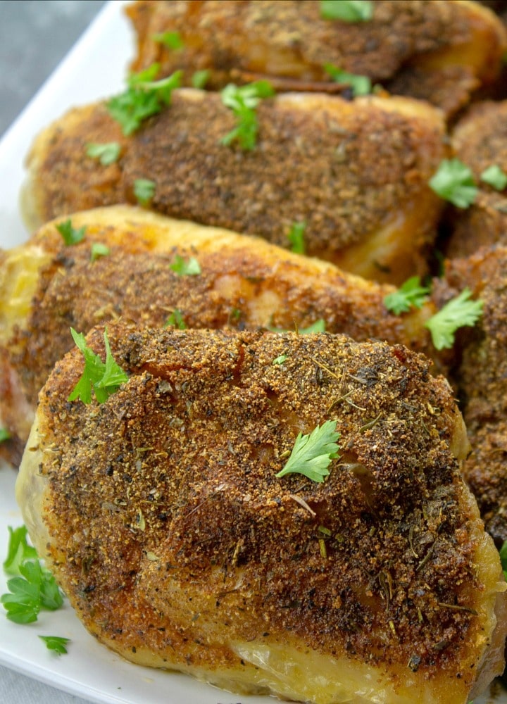 crispy oven baked chicken thigh on white platter with parsley