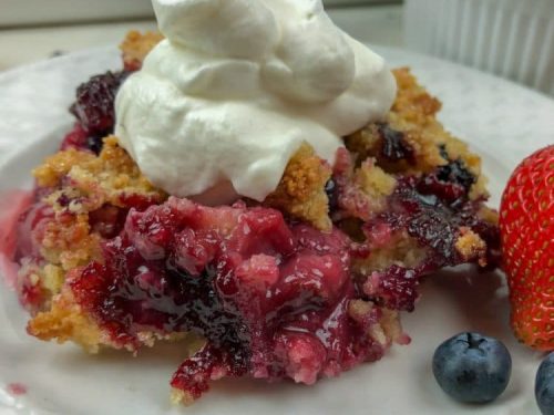 classic berry cobbler with whipped cream on white plate