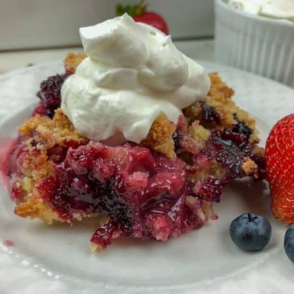 classic berry cobbler with whipped cream on white plate