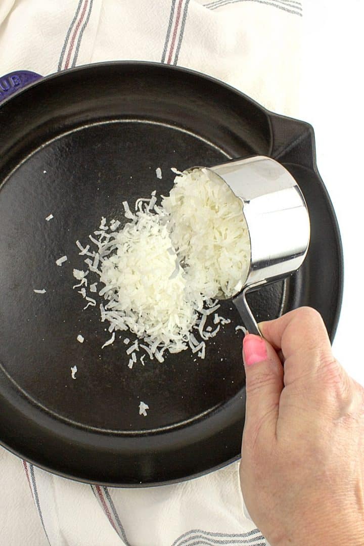 Shredded coconut pouring into cast iron skillet