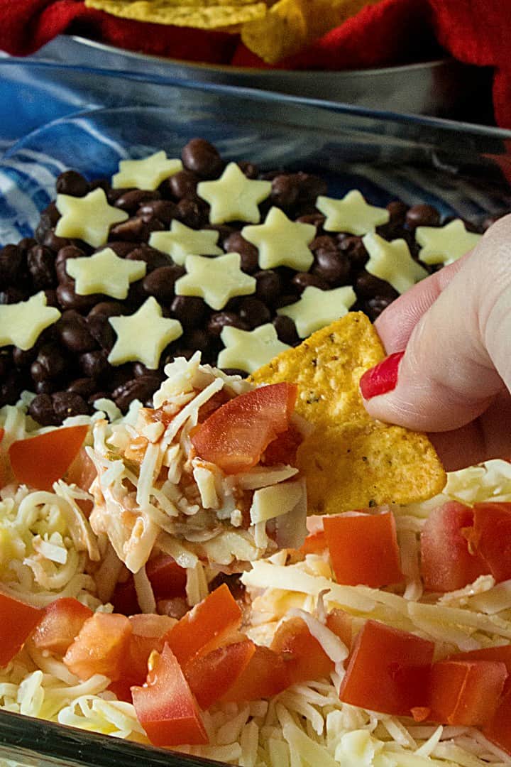 Patriotic Layered Party Dip is a huge hit at summer parties. Seasoned sour cream, black and refried beans, cheese and tomatoes are layered into a zesty 10 minute dip everyone will love! #mustlovehomecooking