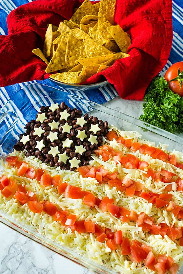 Patriotic Layered Party Dip is a huge hit at summer parties. Seasoned sour cream, black and refried beans, cheese and tomatoes are layered into a zesty 10 minute dip everyone will love! #mustlovehomecooking