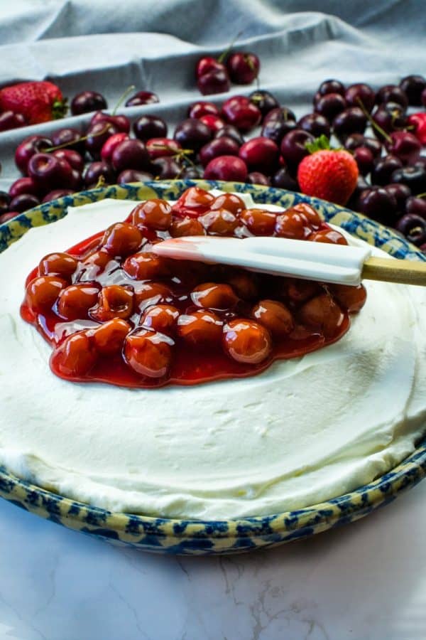 Spreading cherry filling over cheesecake base with a spatula.