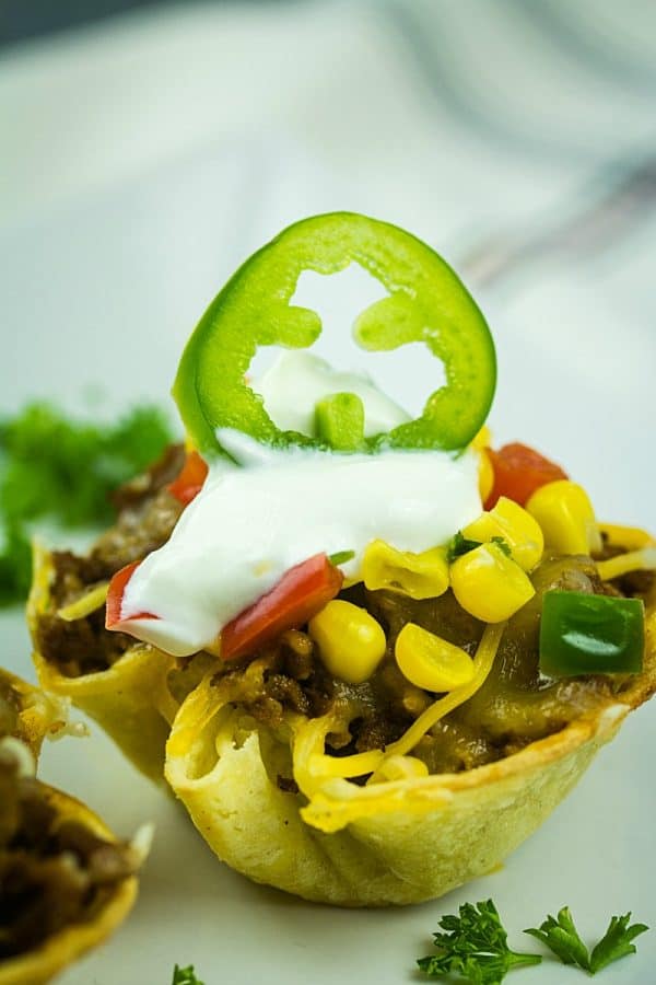 Tortilla taco cups are fun appetizers and a tasty twist on taco night. The layers of seasoned beef and melting cheese are heated in mini corn tortilla cups, then loaded with your favorite taco toppings!