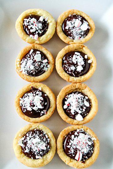 Chocolate Peppermint Sugar Cookie Cups - Tender sugar cookie cups brimming with chocolate ganache filling and crushed peppermint sprinkles! Three holiday favorites in one delicious treat!