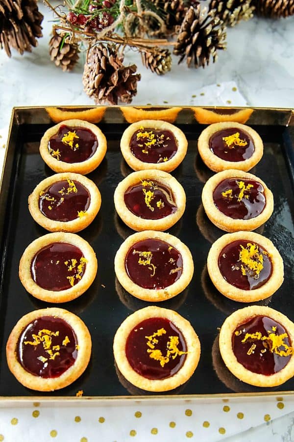 Orange Raspberry Cookie Cups - Buttery orange flavored sugar cookie cups filled with raspberry jam and sprinkled with fresh orange zest. Festive on the cookie tray and easy on the budget.