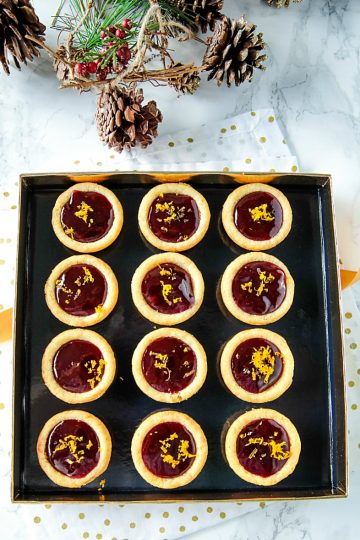 Orange Raspberry Cookie Cups - Buttery orange flavored sugar cookie cups filled with raspberry jam and sprinkled with fresh orange zest. Festive on the cookie tray and easy on the budget.