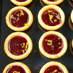 Orange Raspberry Cookie Cups - Buttery orange flavored sugar cookie cups filled with raspberry jam and sprinkled with fresh orange zest. Festive on the cookie tray and easy on the budget.