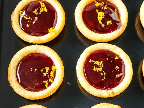 Orange Raspberry Cookie Cups - Buttery orange flavored sugar cookie cups filled with raspberry jam and sprinkled with fresh orange zest. Festive on the cookie tray and easy on the budget.
