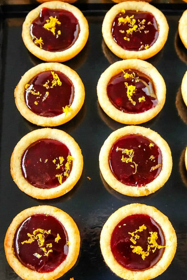 Orange Raspberry Cookie Cups - Buttery orange flavored sugar cookie cups filled with raspberry jam and sprinkled with fresh orange zest. Festive on the cookie tray and easy on the budget.