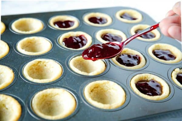 spooning raspberry jam into sugar cookie cups