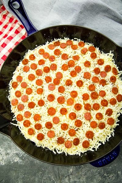 Assembled pizza dip in a blue cast iron skillet.