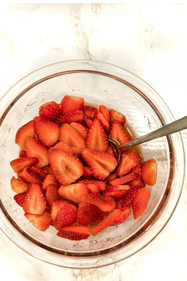 Sliced strawberries in a glass mixing bowl.