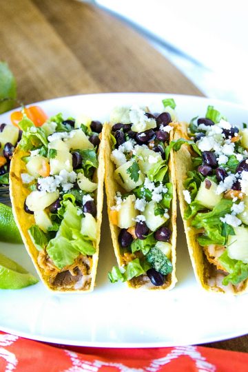 Easy Oven Chicken Tacos are seasoned shredded chicken stuffed into refried bean smeared crunchy shells and topped with cheese. Baked easy in the oven then loaded with spoonfuls of fresh pineapple salsa.