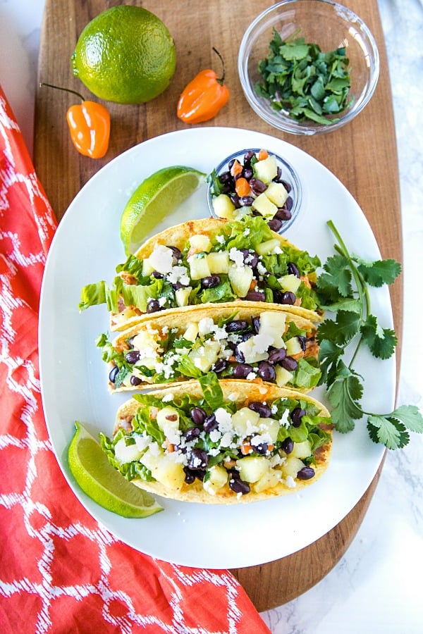 Easy Oven Chicken Tacos are seasoned shredded chicken stuffed into refried bean smeared crunchy shells and topped with cheese. Baked easy in the oven then loaded with spoonfuls of fresh pineapple salsa. #mustlovehomecooing #chickentacos #mexicanfood