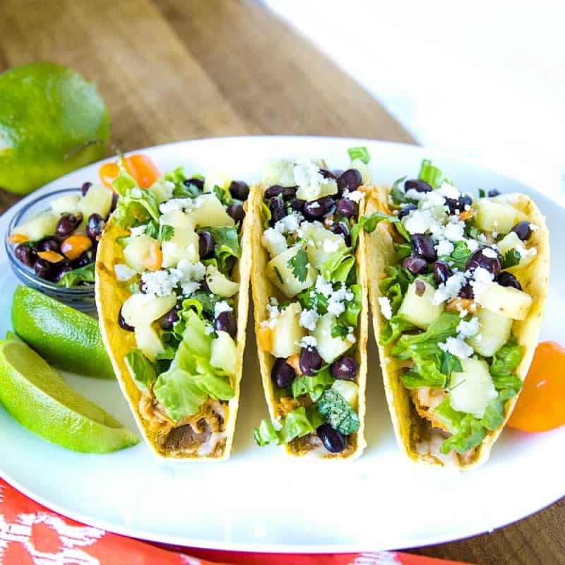 Easy Oven Chicken Tacos are seasoned shredded chicken stuffed into refried bean smeared crunchy shells and topped with cheese. Baked easy in the oven then loaded with spoonfuls of fresh pineapple salsa. #mustlovehomecooking #tacorecipe #mexicanfood