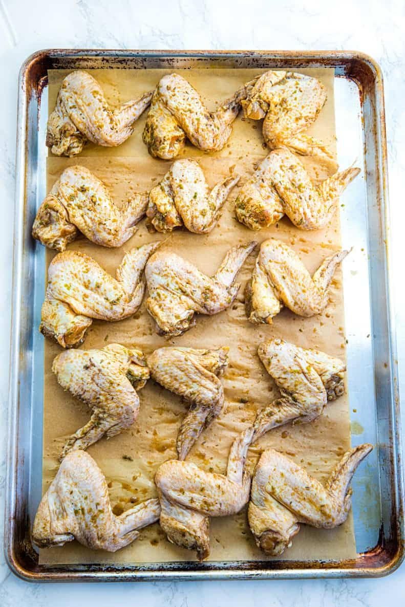 Marinated chicken wings on a sheet pan with parchment paper ready for the oven.