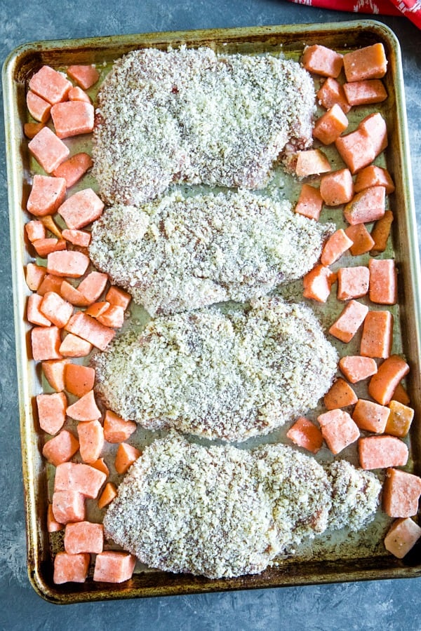 Pank crumb coated pork chops and sweet potatoes on sheet pan ready for the oven