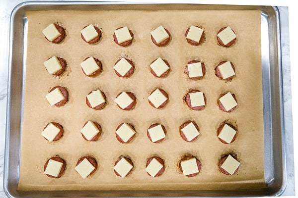 baked smoked sausage with cheese cube on parchment sheet on sheet pan