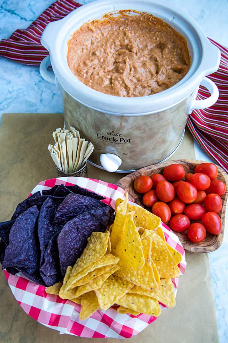 Creamy hot bean dip is loaded with refried beans, melted cheese, silky sour cream, and zesty spices. It's made in the slow cooker for easy, stay-warm serving or the oven for luscious cheese on top! #mustlovehomecooking