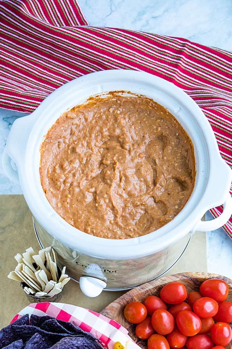 Creamy hot bean dip is loaded with refried beans, melted cheese, silky sour cream, and zesty spices. It's made in the slow cooker for easy, stay-warm serving or the oven for luscious cheese on top! #mustlovehomecooking