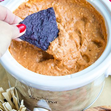 Creamy hot bean dip is loaded with refried beans, melted cheese, silky sour cream, and zesty spices. It's made in the slow cooker for easy, stay-warm serving or the oven for luscious cheese on top! #mustlovehomecooking