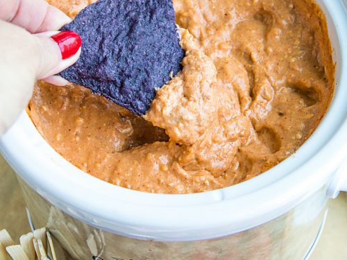 Creamy hot bean dip is loaded with refried beans, melted cheese, silky sour cream, and zesty spices. It's made in the slow cooker for easy, stay-warm serving or the oven for luscious cheese on top! #mustlovehomecooking