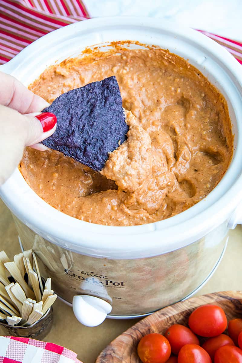 Creamy hot bean dip is loaded with refried beans, melted cheese, silky sour cream, and zesty spices. It's made in the slow cooker for easy, stay-warm serving or the oven for luscious cheese on top! #mustlovehomecooking